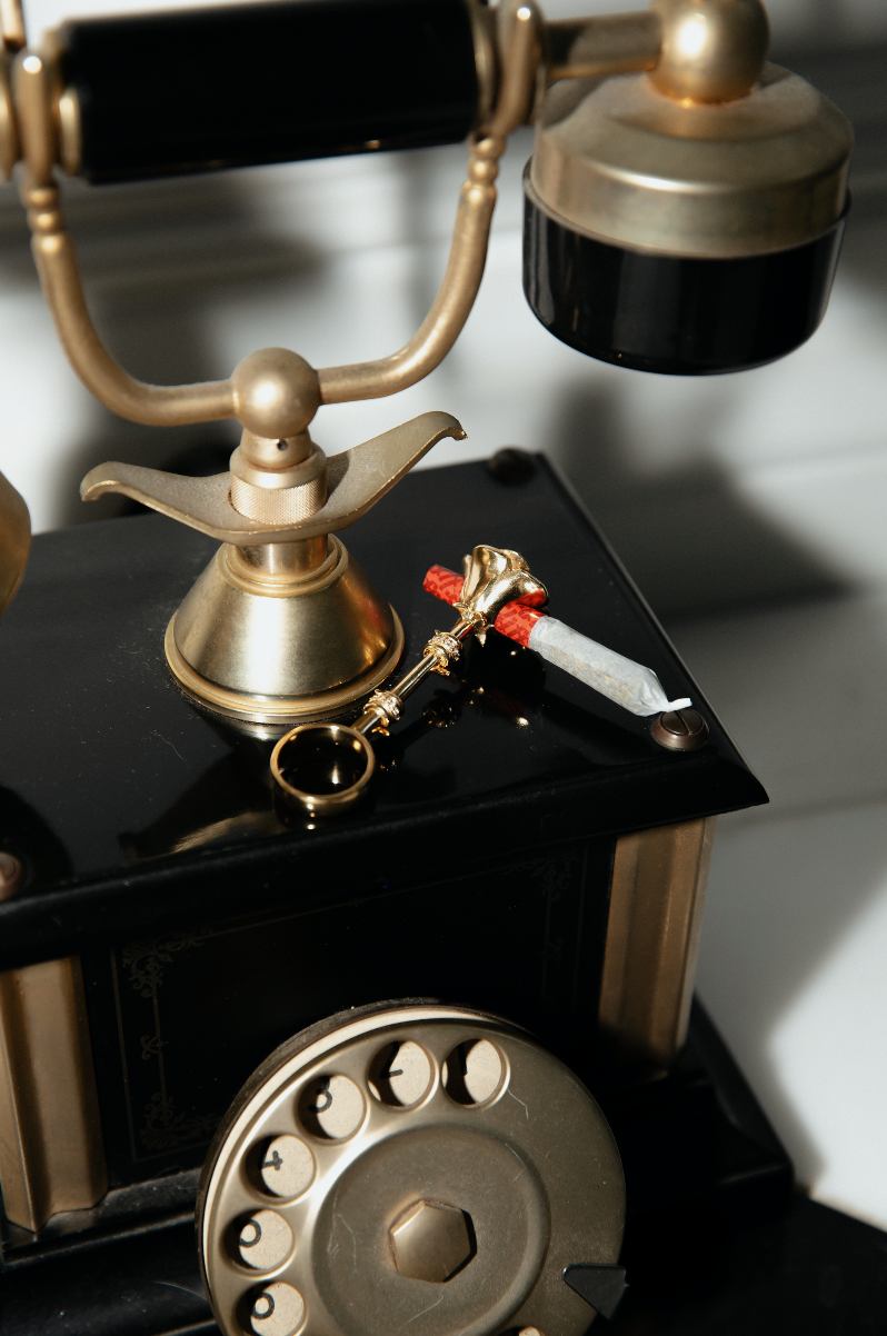 The Farewell Rose Fumette Ring in gold holding a joint on a rotary phone.
