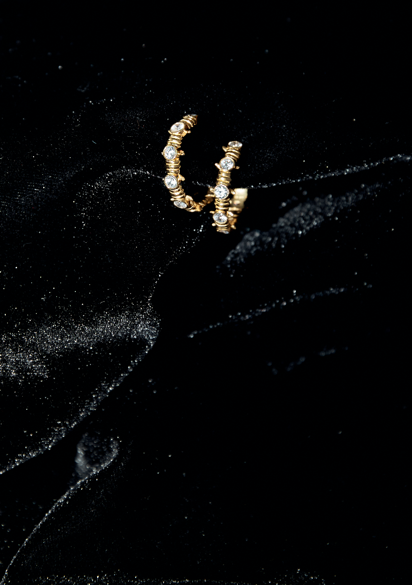 Caught Up Earrings in gold with clear crystal details on a black velvet background.